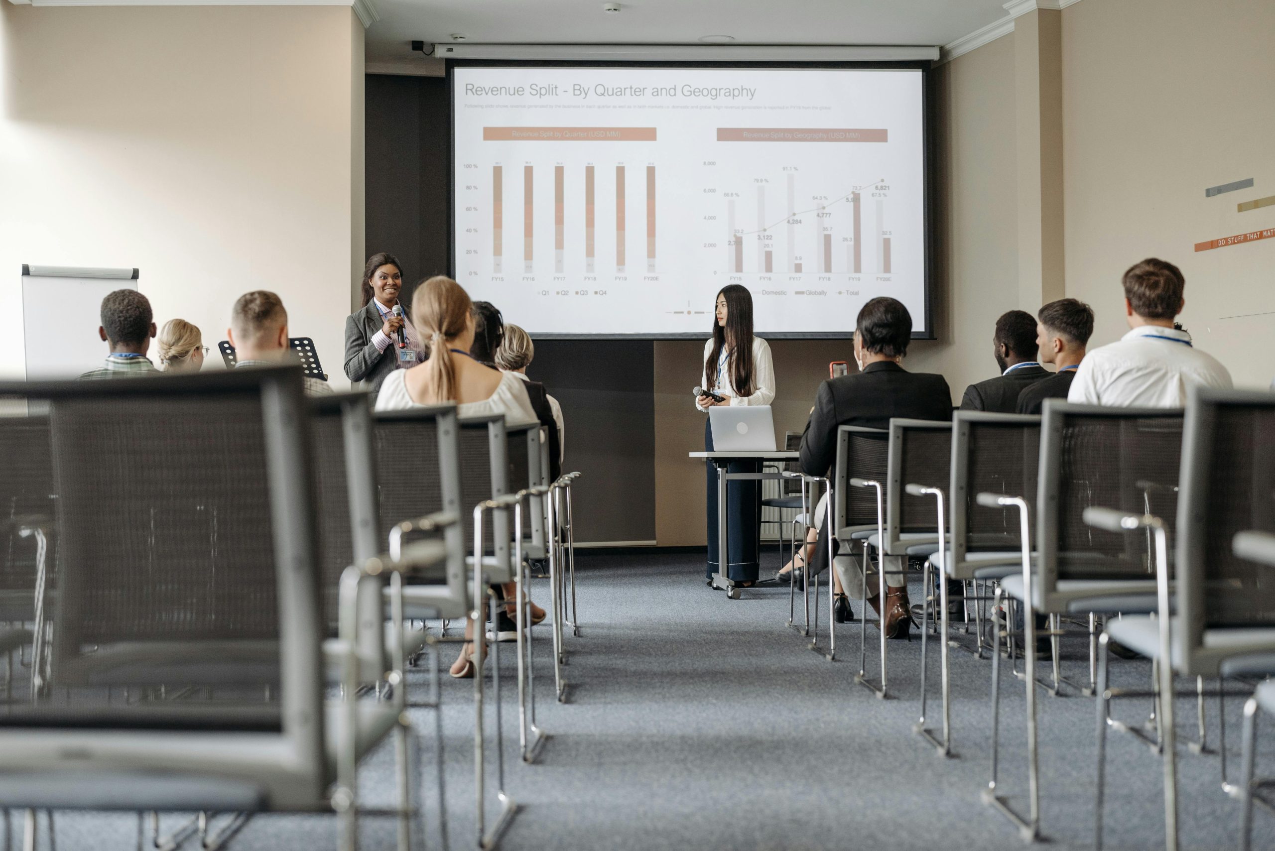 Business conference attendees listen to a presentation on revenue split by quarter and geography.