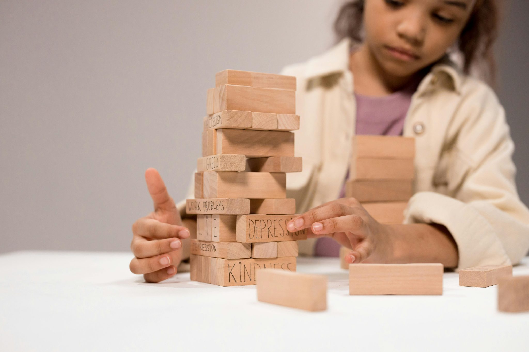 A child thoughtfully stacks wooden blocks with words like 'depression' and 'kindness.'