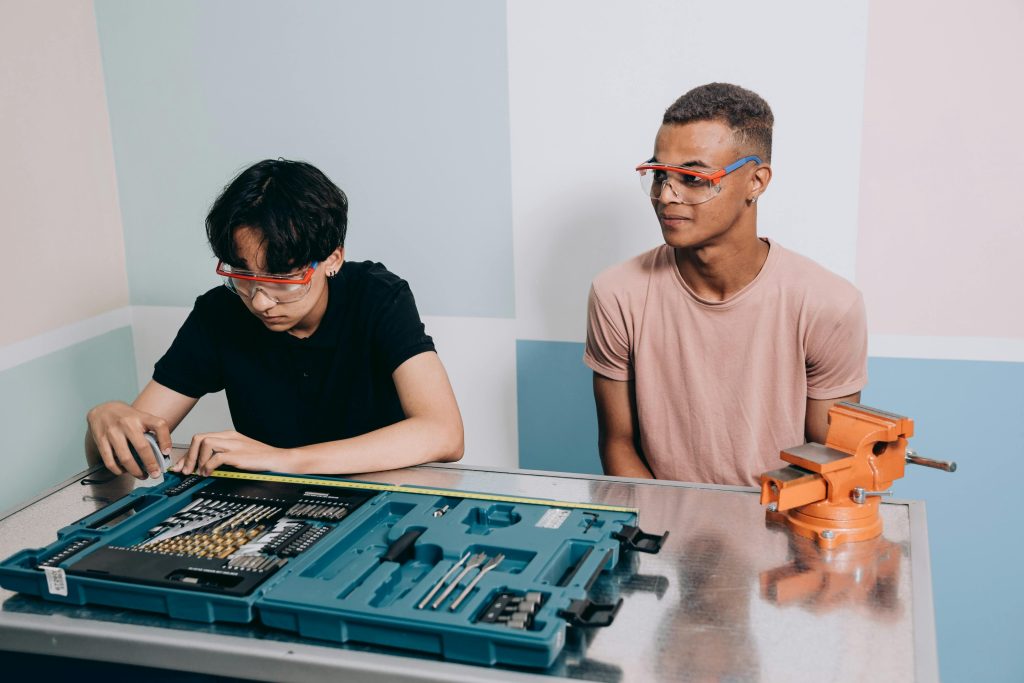 Two young men with safety glasses working on a project with tools indoors.